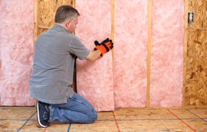 Technician installing pink batt fiberglass insulation in an unfinished wall.