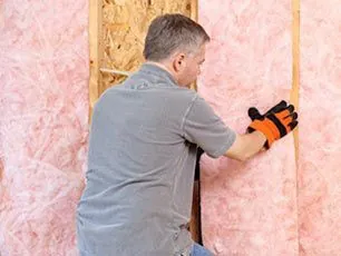 Technician installing pink fiberglass batt insulation in a wall