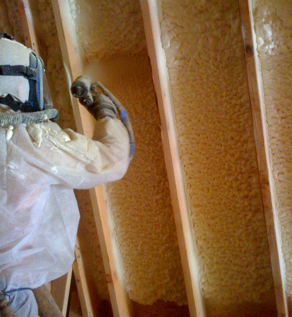 Technician in hazmat suit, applying spray foam insulation to an unfinished wall. 