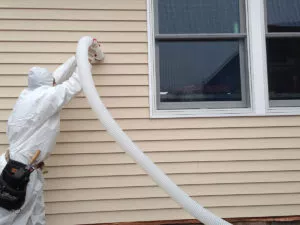 Technician installing wall insulation from outside a home.
